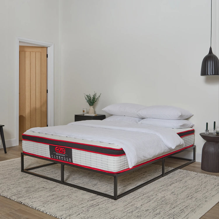 Bed with white bedding and red accent on a wooden floor in a room with a door and lamp.