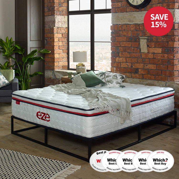 White mattress with red accents on a metal frame in a room with brick walls and large windows.