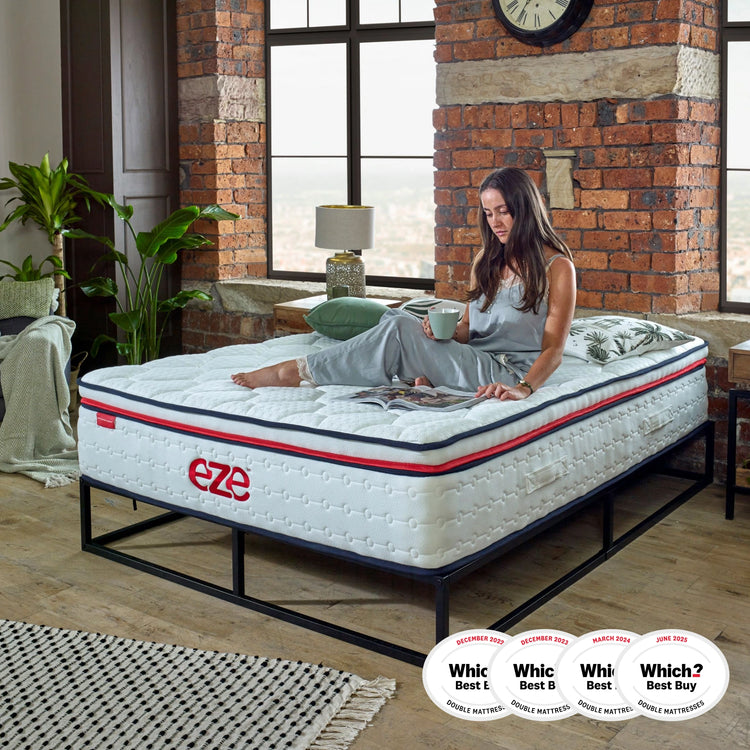 women sat on eze hybrid max mattress reading a magazine on a black metal bedframe with underbed storage against an exposed brick wall with 4 which logos