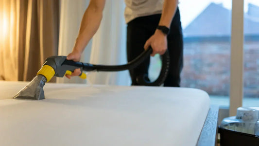 a man stood over a bed holding a hoover and hoovering the surface of the mattress 
