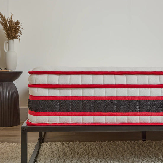 Red and white mattress on a metal frame against a neutral wall.