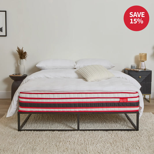 Mattress on a bed frame with decorative pillows and a tray, in a room setting.