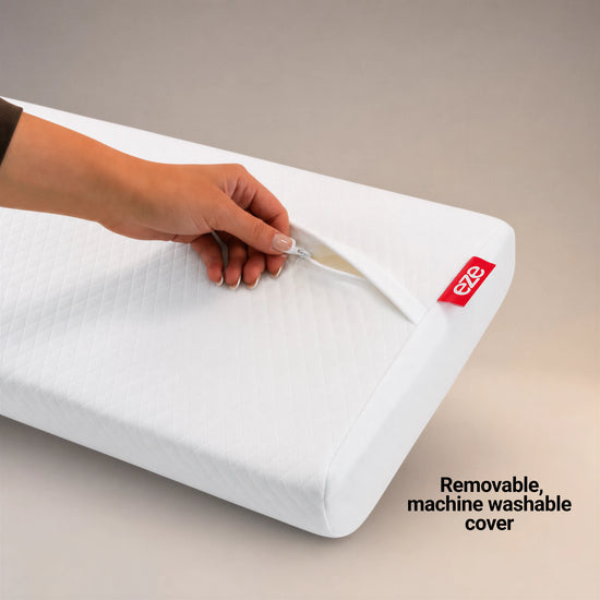 A white quilted pillow with a removable, machine-washable cover, shown with a hand unzipping the corner. A red tag on the pillow displays the 'eze' brand logo.