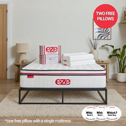 A white Eze mattress on a black metal bed frame in a styled bedroom setting, with two white pillows, an Eze product box, a red 'Two Free Pillows' badge, and a Which? Best Buy badge. Text at the bottom reads '*one free pillow with a single mattress'.